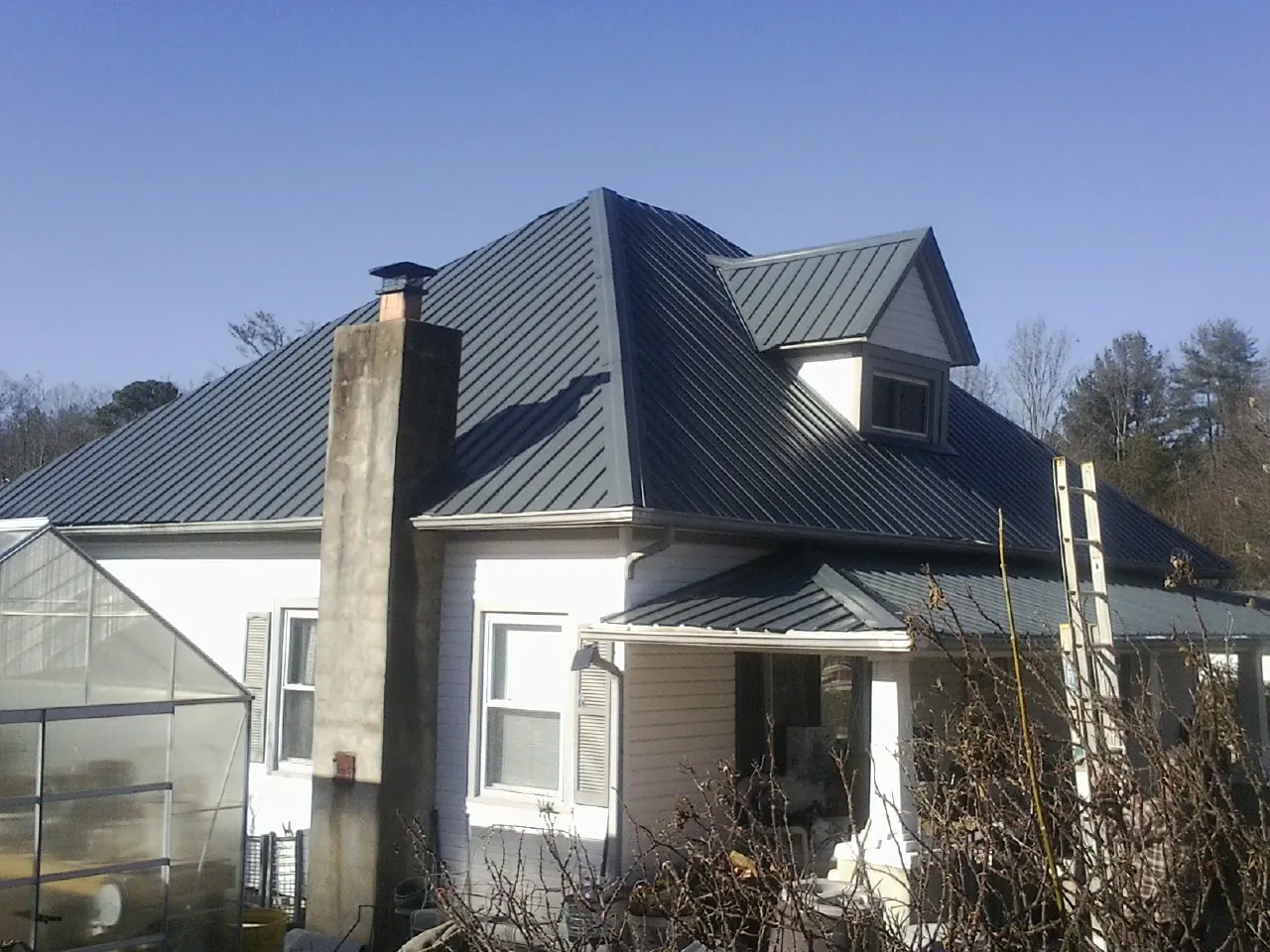 Dark blue standing seam metal roof on a white farmhouse with dormer — Slate & Tile Roof Repair by Roofing Brothers in Biscoe