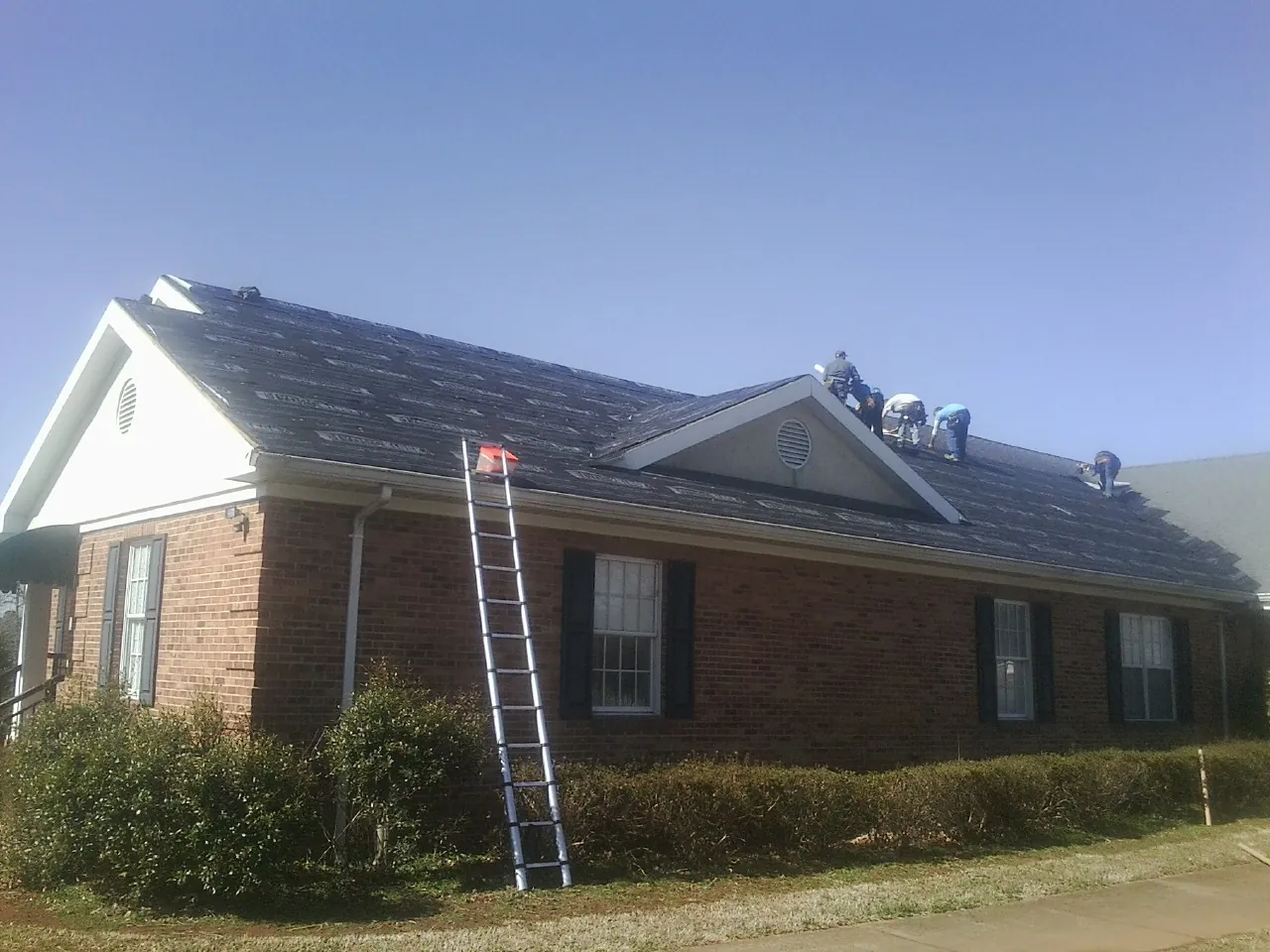 Crew tearing shingles off a brick ranch roof with a ladder set — Metal Roof Repair work by our crew in Biscoe