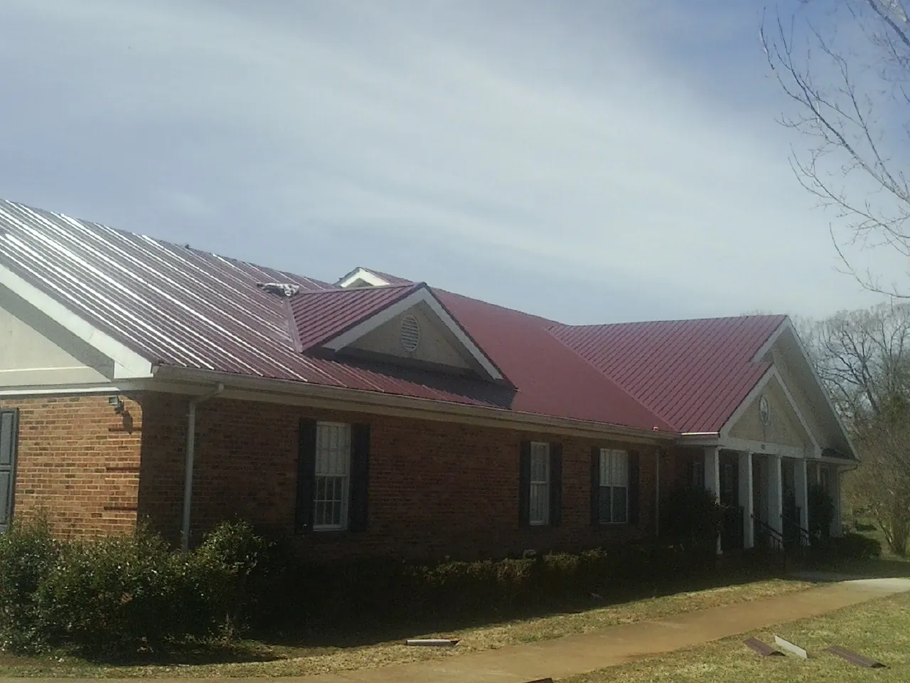 Red metal roof with gabled entries on a long brick building, from a Hail Damage Roof Repair job in Biscoe