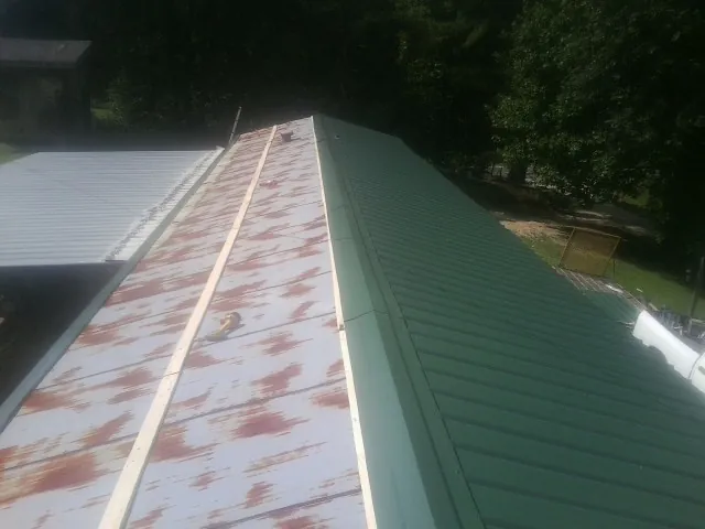 Old rusted panels beside newly installed green metal roofing — Wind Damage Roof Repair by Roofing Brothers in Biscoe