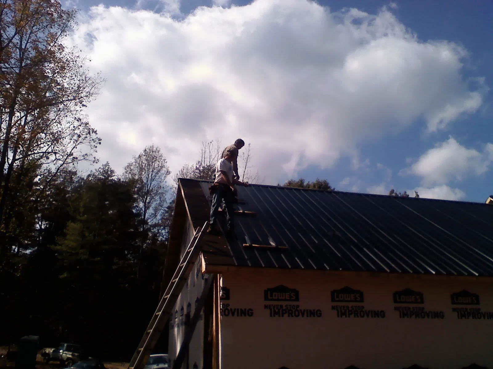 Roofer fastening dark metal panels high against a cloudy sky, from a Roof Inspection job in Biscoe