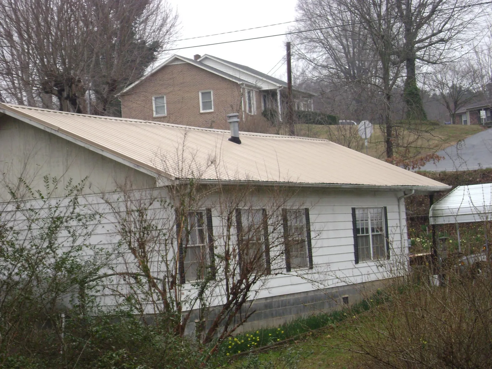 Tan metal roof on a white sided house set into a hillside — Commercial Roofing by Roofing Brothers in Biscoe