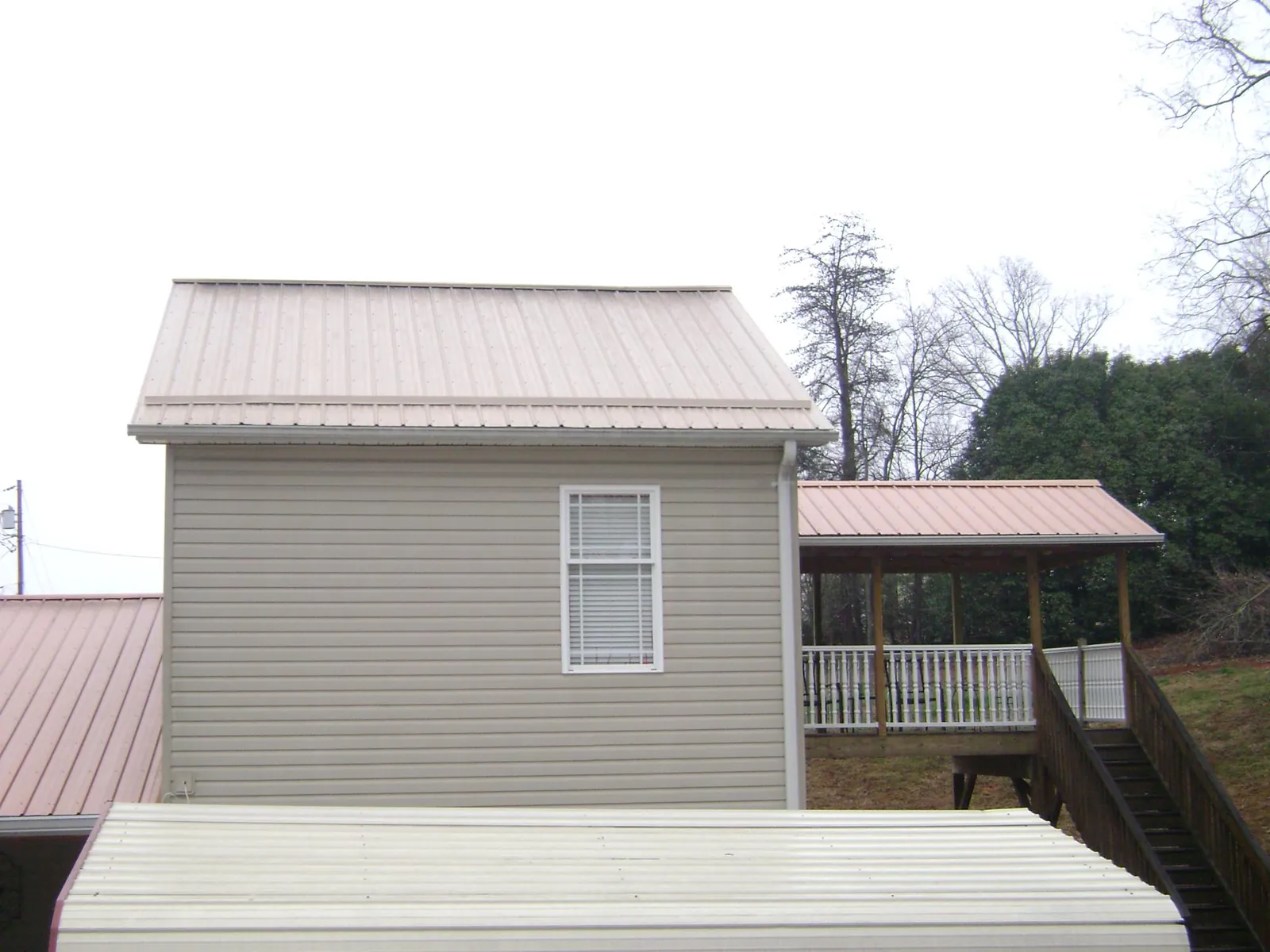 Tan metal roofs on a two story addition and attached porch, from a Roof Replacement job in Biscoe